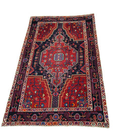 A rectangular vintage Persian rug featuring a geometric red and navy blue medallion pattern.