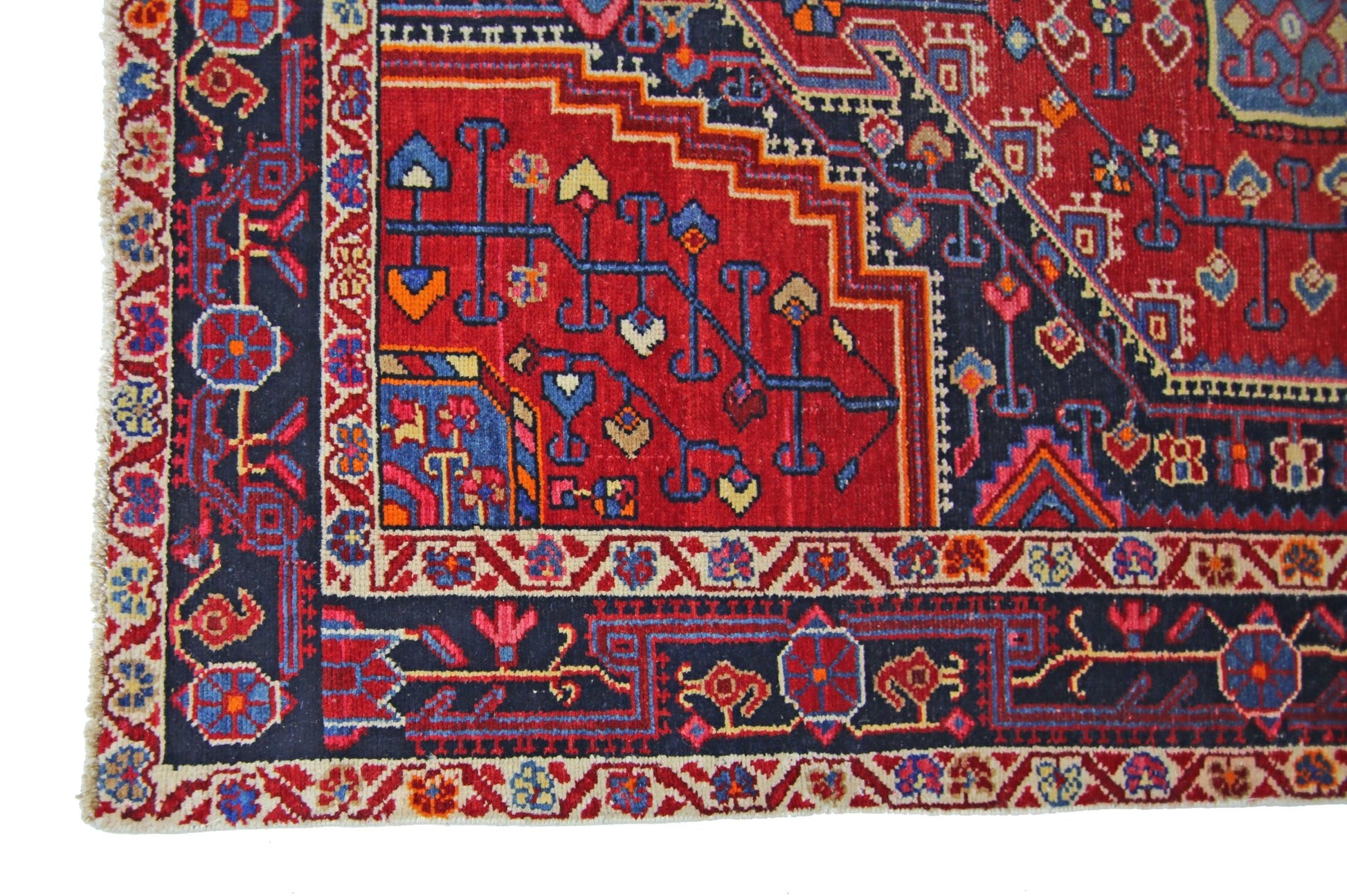 A vintage handmade Persian rug featuring intricate geometric patterns in red, blue, and cream.