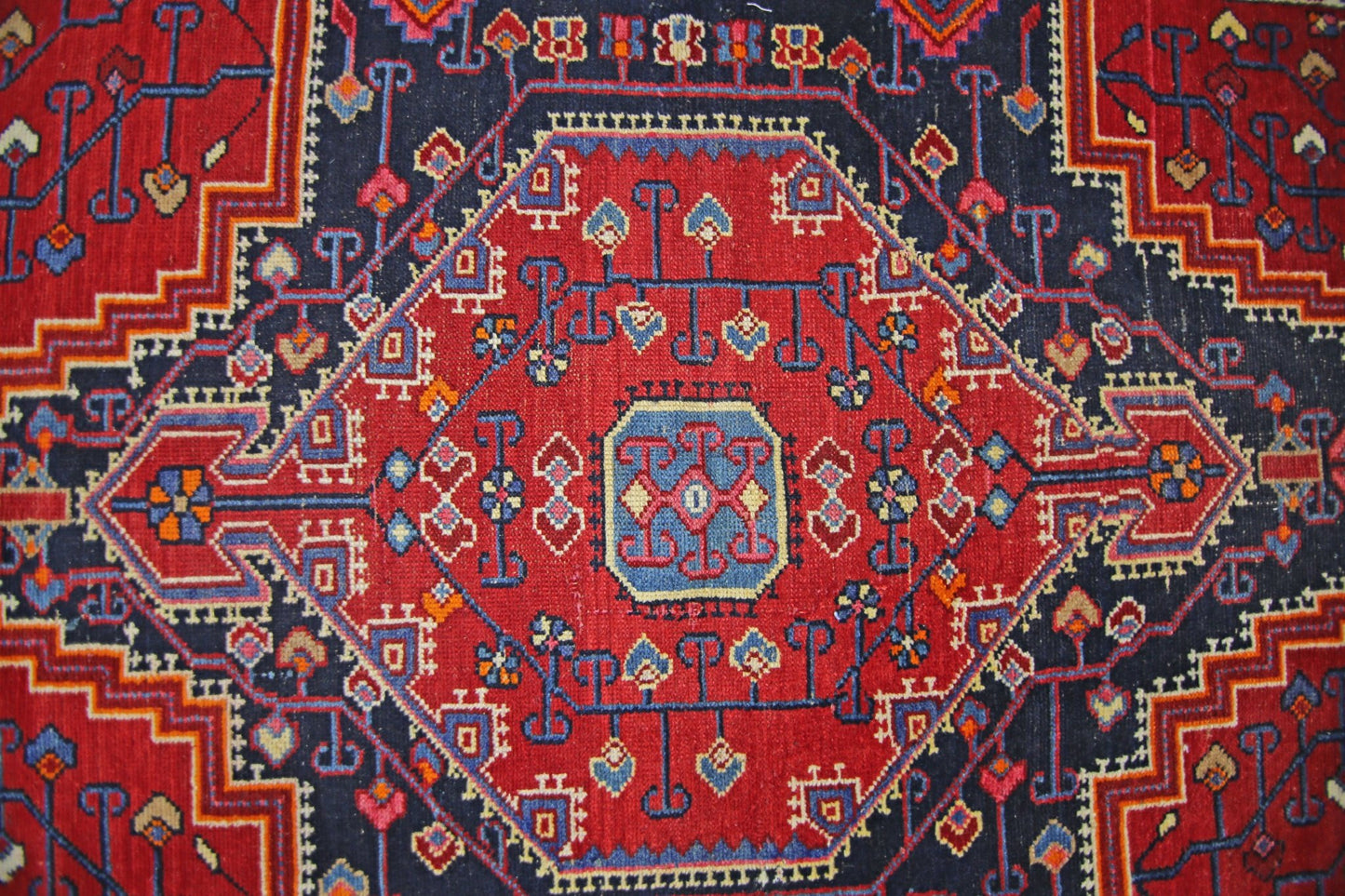 A vintage Persian rug featuring a geometric red diamond medallion on a dark blue background.