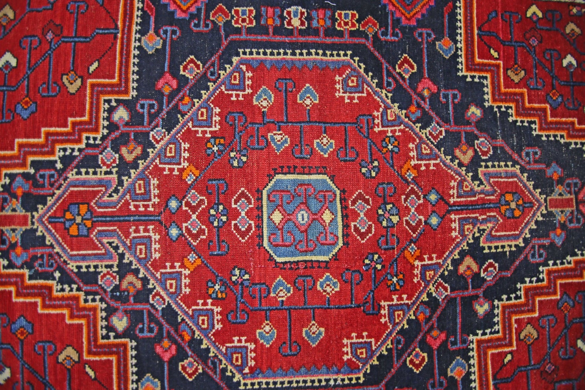 A vintage Persian rug featuring a geometric red diamond medallion on a dark blue background.