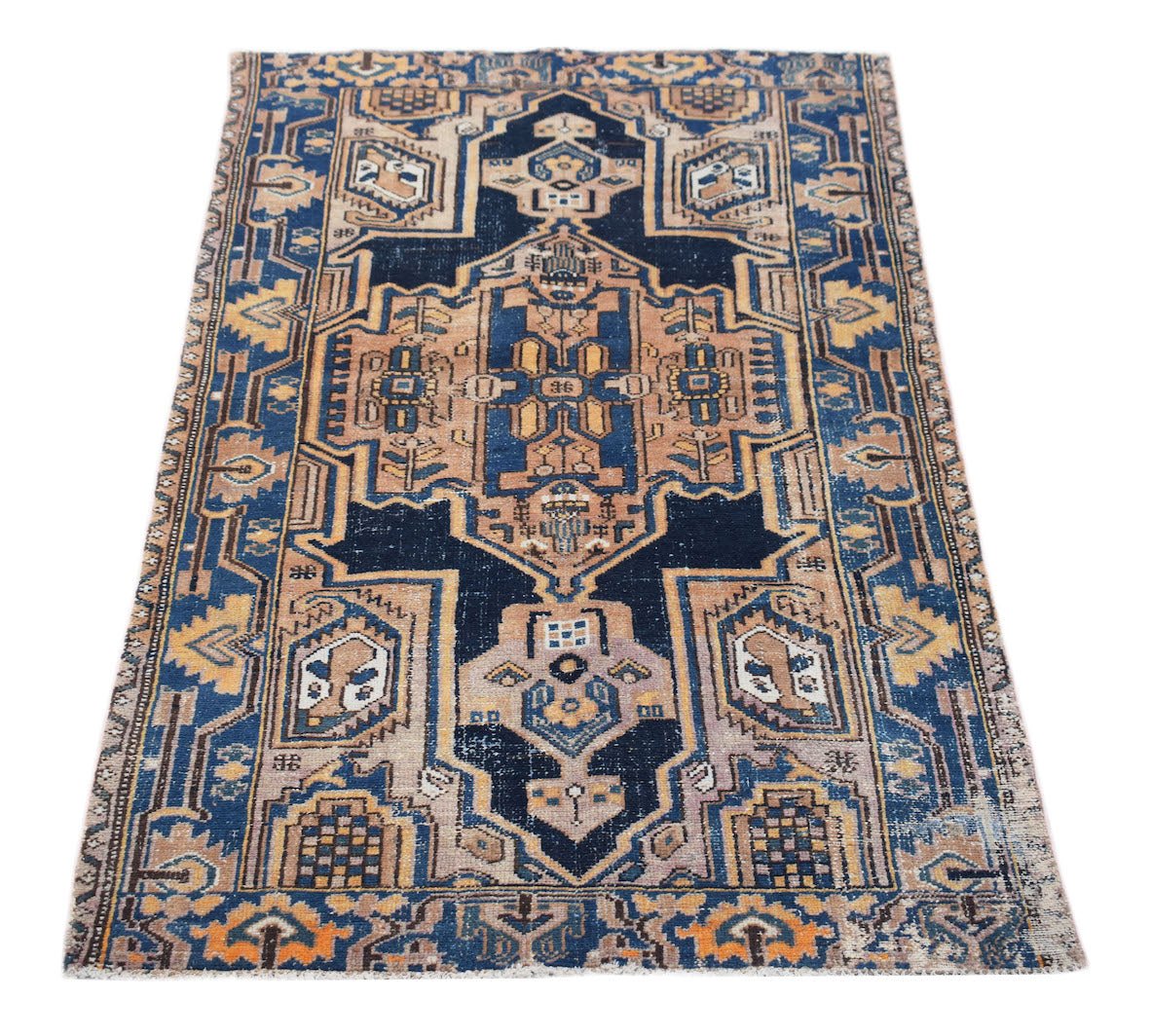 A vintage handwoven Persian rug featuring a geometric pattern in shades of blue, tan, and gold.