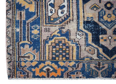 A handwoven vintage Persian rug featuring intricate geometric patterns in blue, tan, and orange.