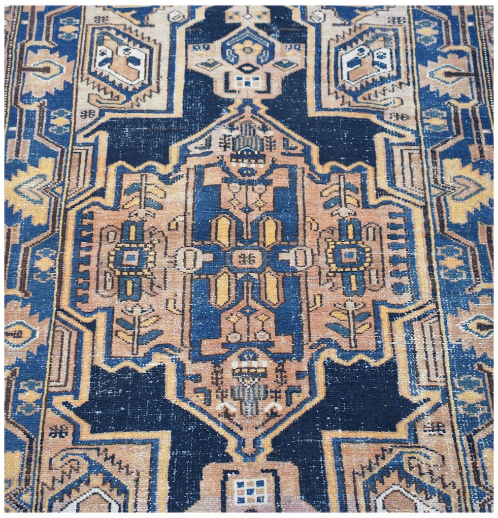 A vintage handwoven Persian rug featuring a geometric medallion pattern in blue and tan tones.