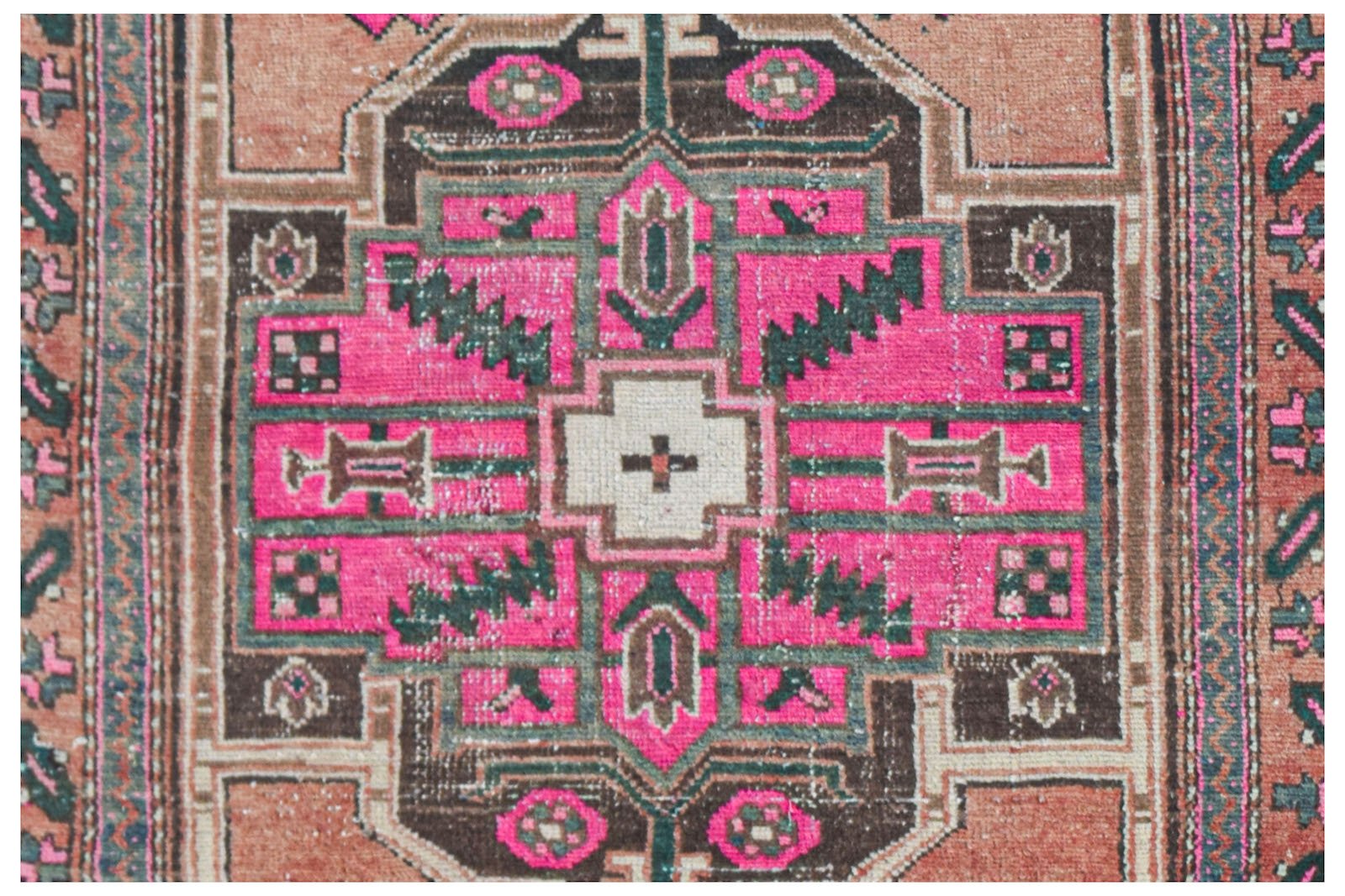 A vintage handwoven Persian rug featuring a geometric central medallion in pink, brown, and cream.