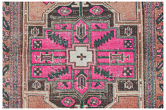A vintage handwoven Persian rug featuring a geometric central medallion in pink, brown, and cream.