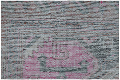 A close-up of a vintage handwoven Persian rug featuring a distressed pattern in pink and grey.
