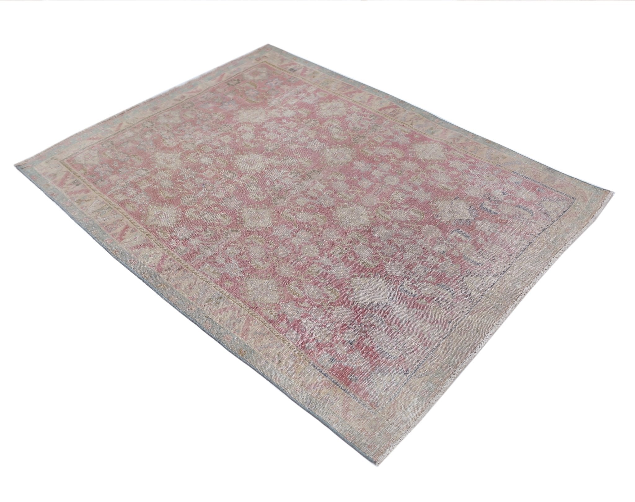 A vintage handmade Persian rug featuring a faded pink and beige floral pattern.