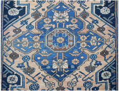 A vintage handwoven Persian rug featuring a blue central medallion on a peach field with floral motifs.