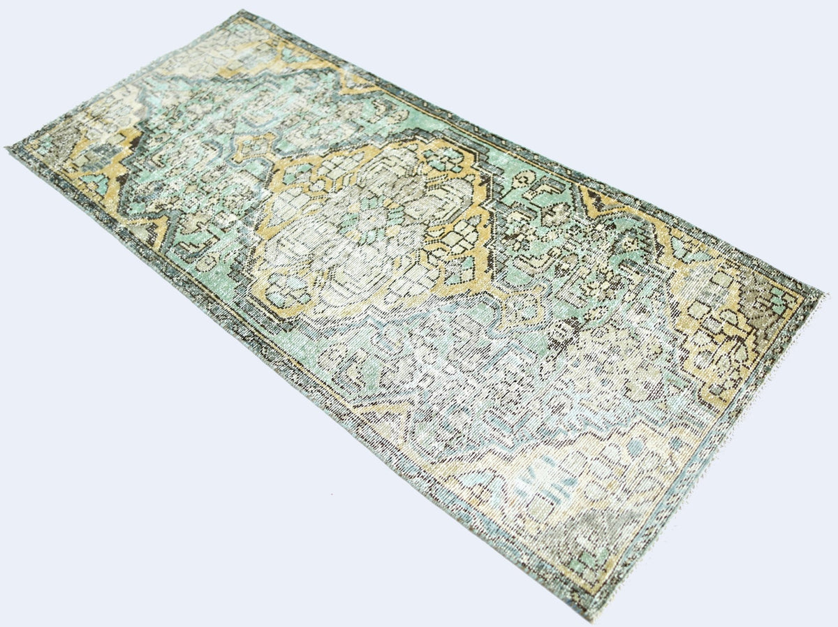 A vintage handmade Persian rug featuring a distressed floral pattern in shades of teal and gold.