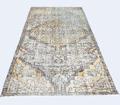 A vintage Persian rug featuring a distressed geometric pattern in shades of yellow, blue, and brown.