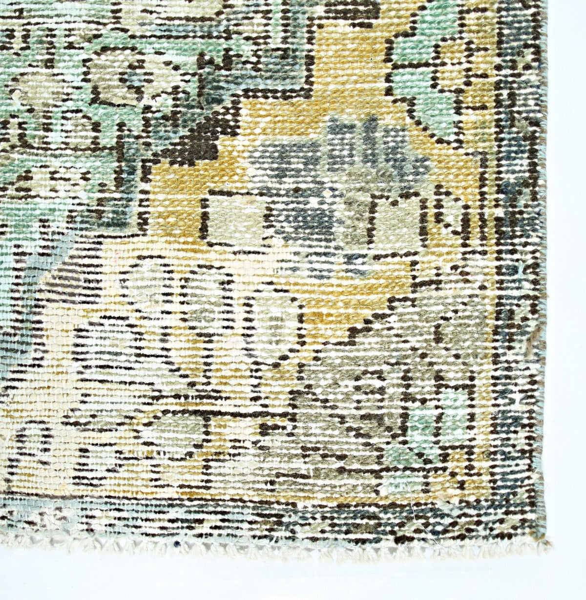 A close-up of a vintage Persian rug featuring a distressed floral pattern in muted green and gold.