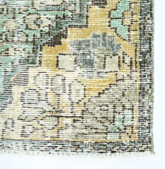 A close-up of a vintage Persian rug featuring a distressed floral pattern in muted green and gold.