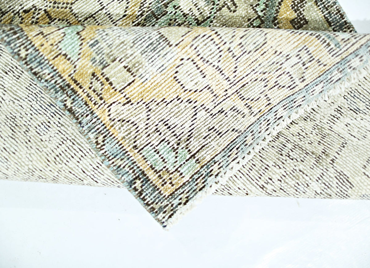 A folded vintage Persian rug featuring a faded geometric pattern in muted tones.