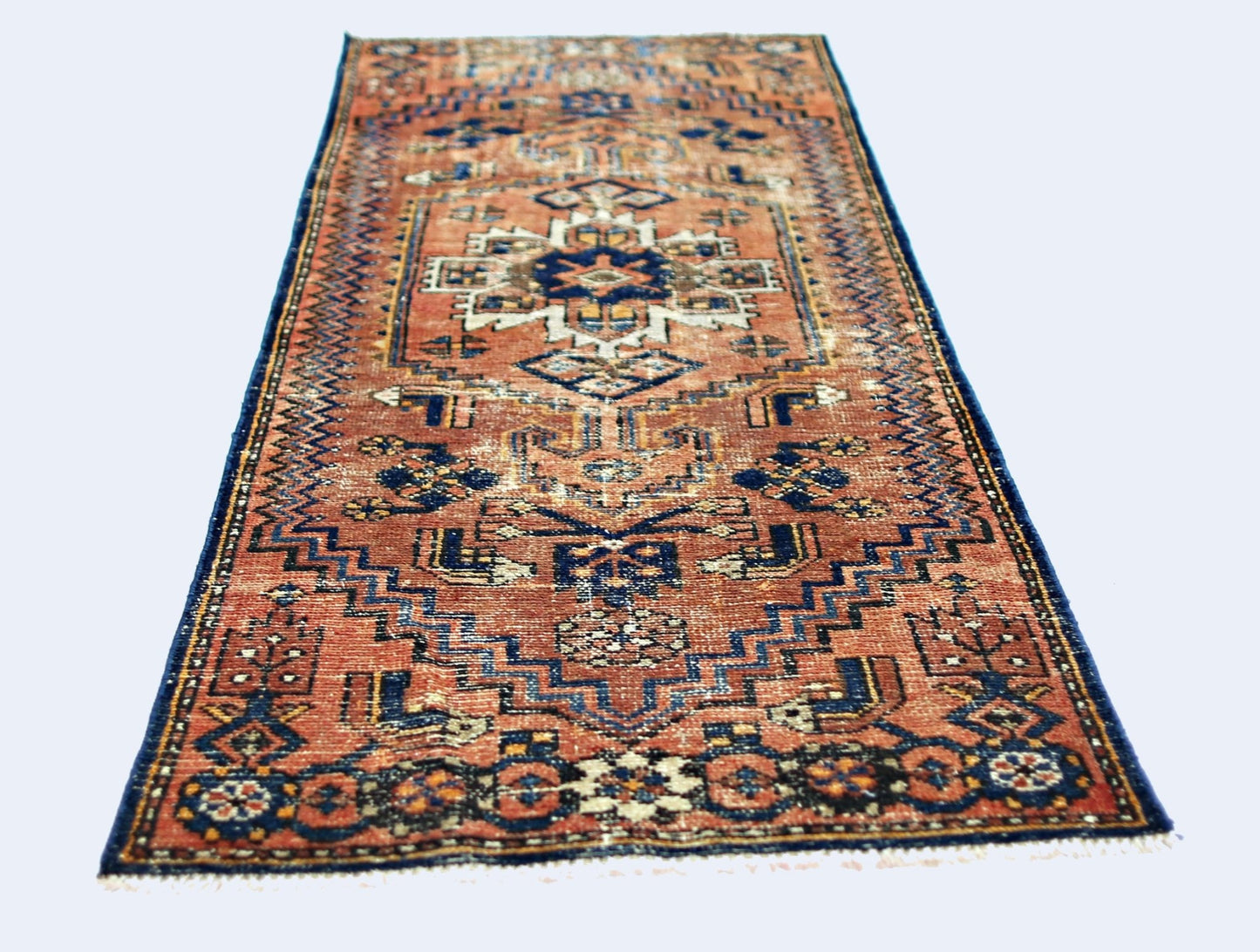 A vintage handmade Caucasian runner rug featuring a geometric pattern in rust and blue tones.