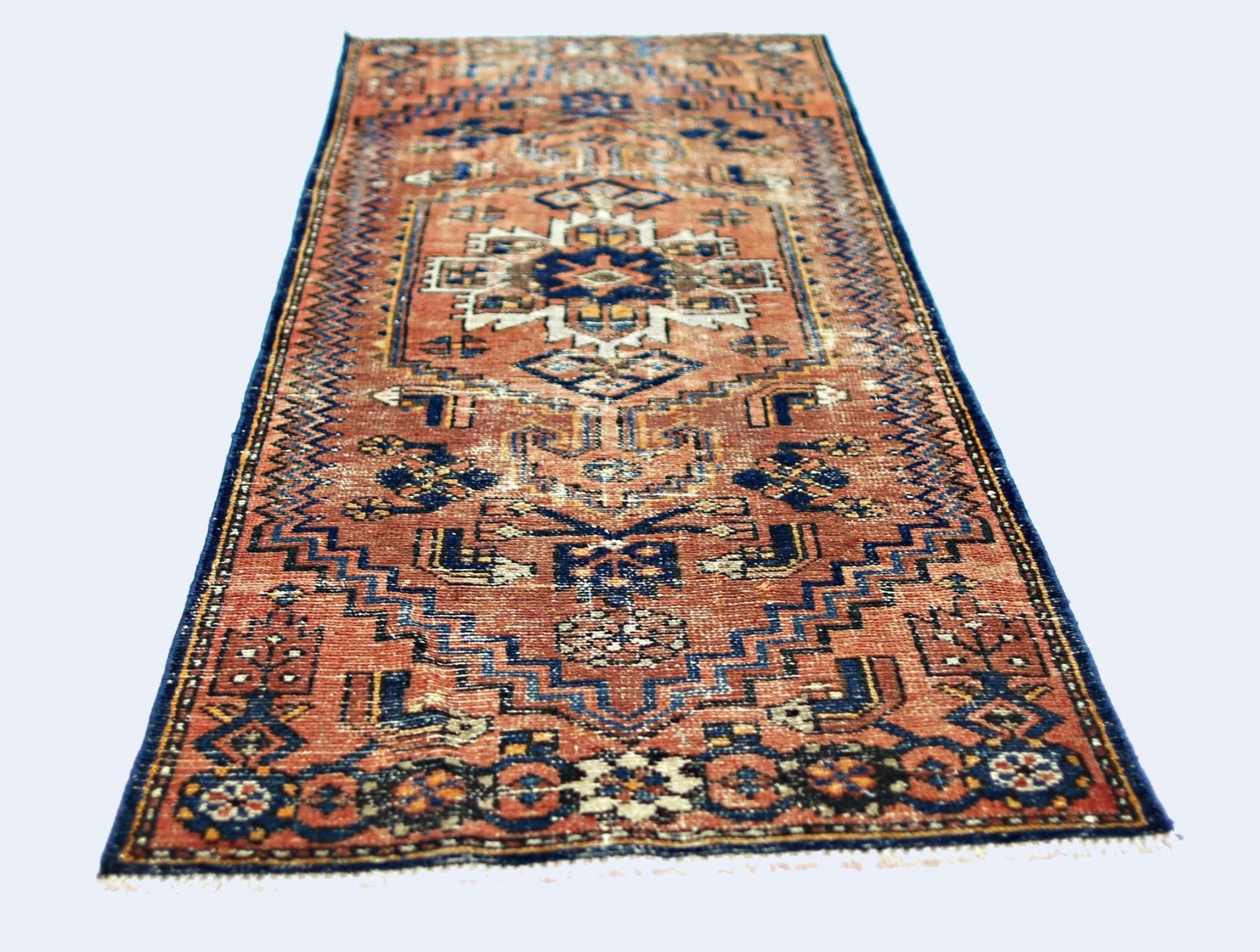 A vintage handmade Caucasian runner rug featuring a geometric pattern in rust and blue tones.
