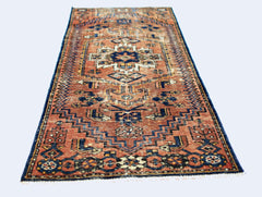 A vintage handmade Caucasian runner rug featuring a geometric pattern in rust and blue tones.