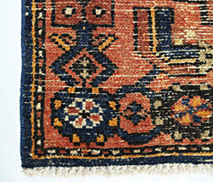 A vintage handmade Persian rug featuring geometric floral patterns in red, blue, and orange wool.