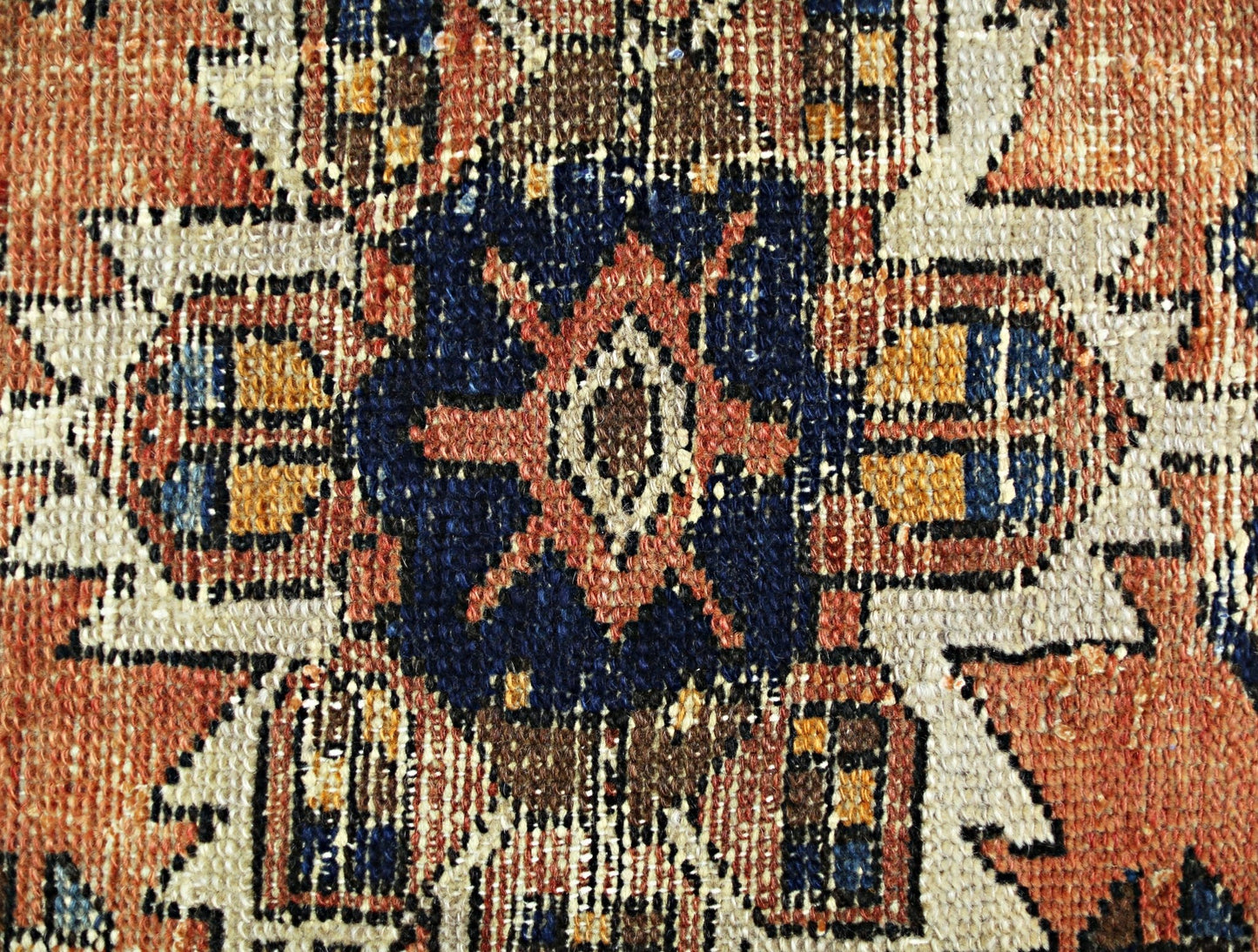 A close-up of a vintage Persian rug featuring a geometric floral medallion in blue and orange.