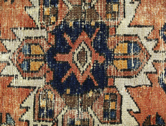 A close-up of a vintage Persian rug featuring a geometric floral medallion in blue and orange.
