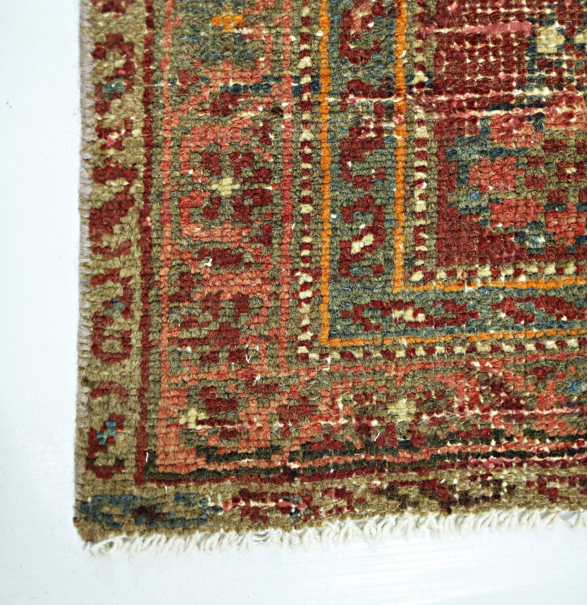 A close-up of a handmade vintage Persian rug featuring intricate geometric patterns in red and green.