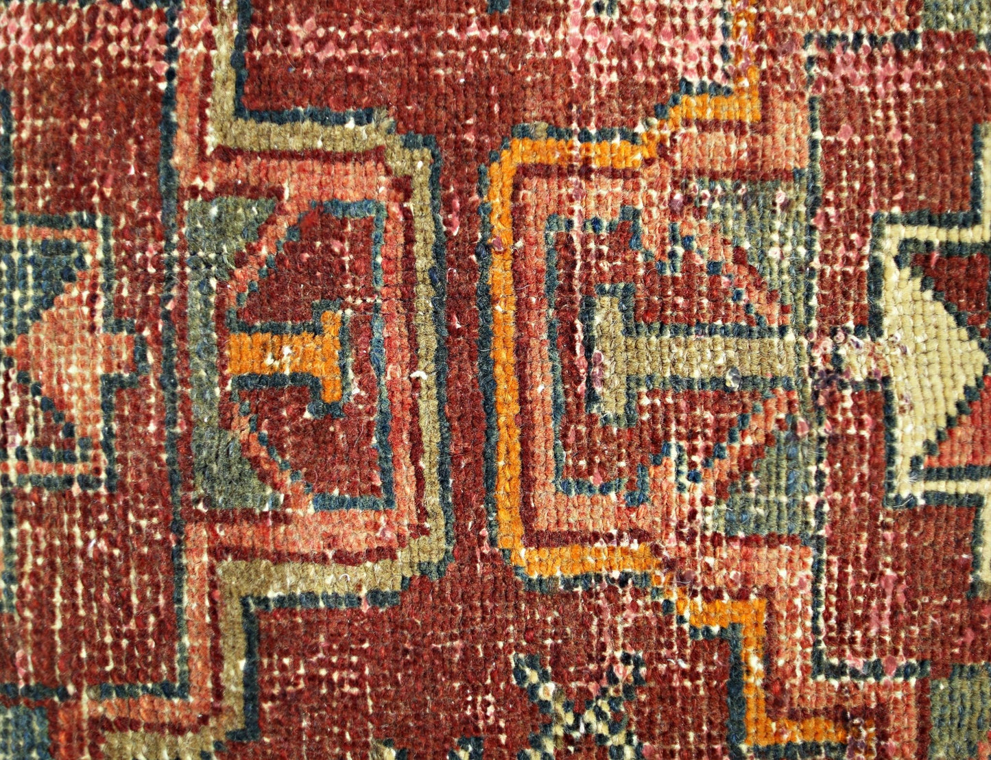 A close-up of a vintage Persian rug featuring geometric patterns in red, orange, and blue wool.