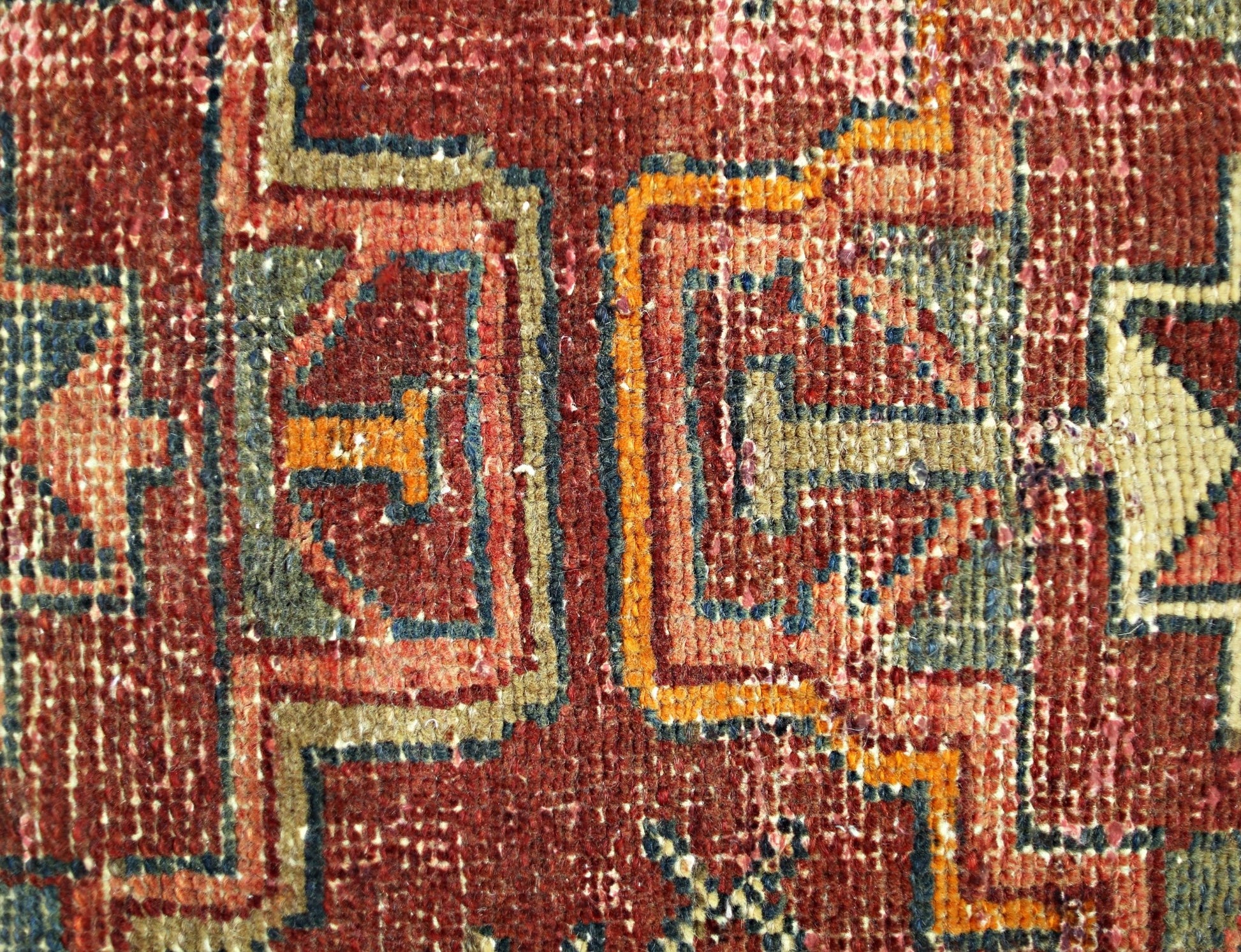 A close-up of a vintage Persian rug featuring geometric patterns in red, orange, and blue wool.