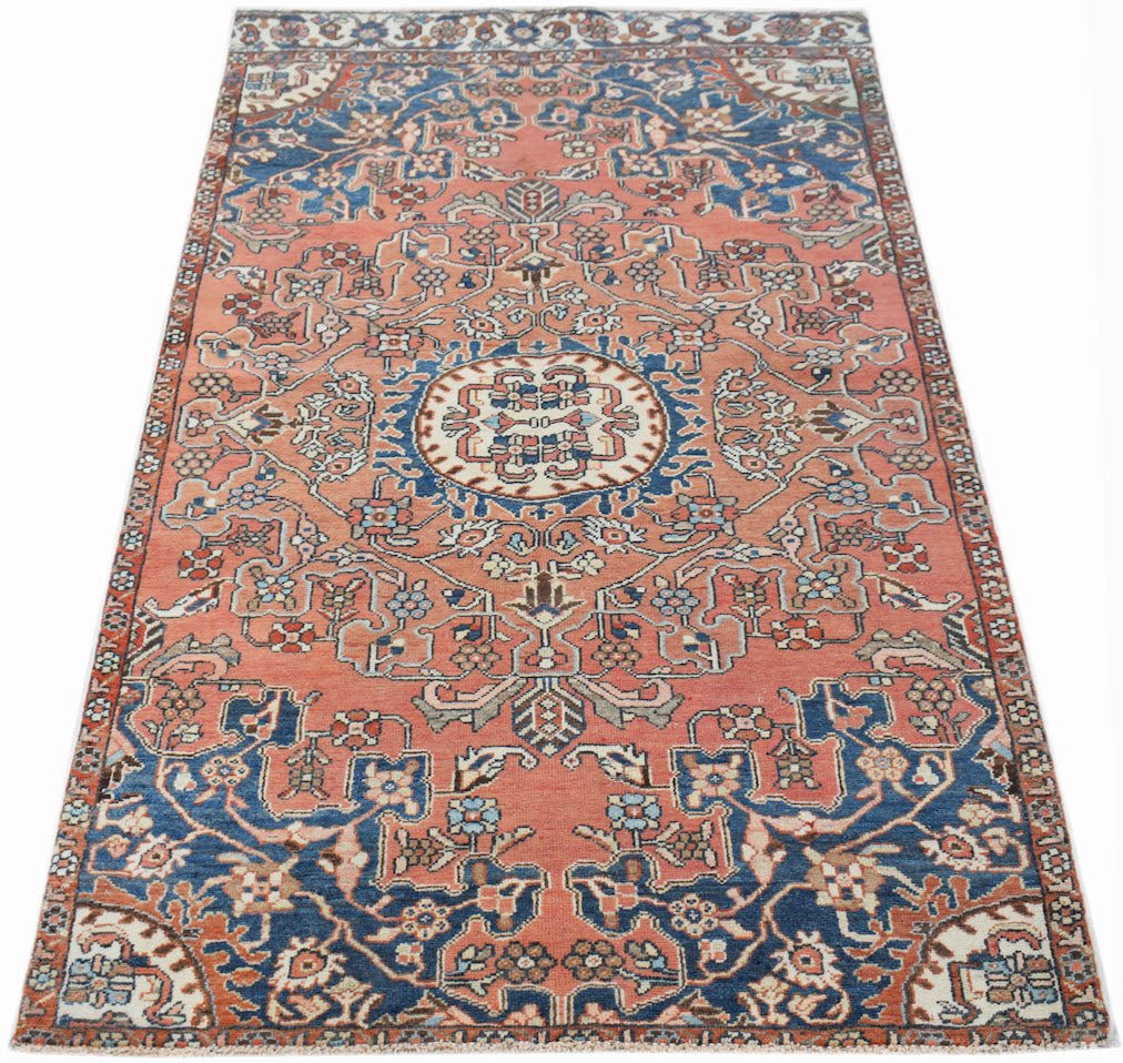 A vintage handwoven Persian rug featuring a floral pattern in shades of coral and blue.