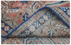 A vintage handwoven Persian rug featuring a faded floral pattern in shades of blue and coral.