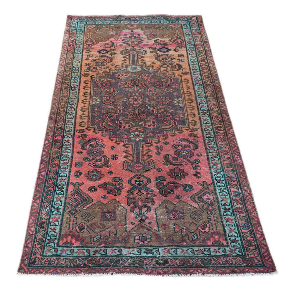 A vintage handwoven Persian rug featuring a central medallion in shades of pink, brown, and teal.