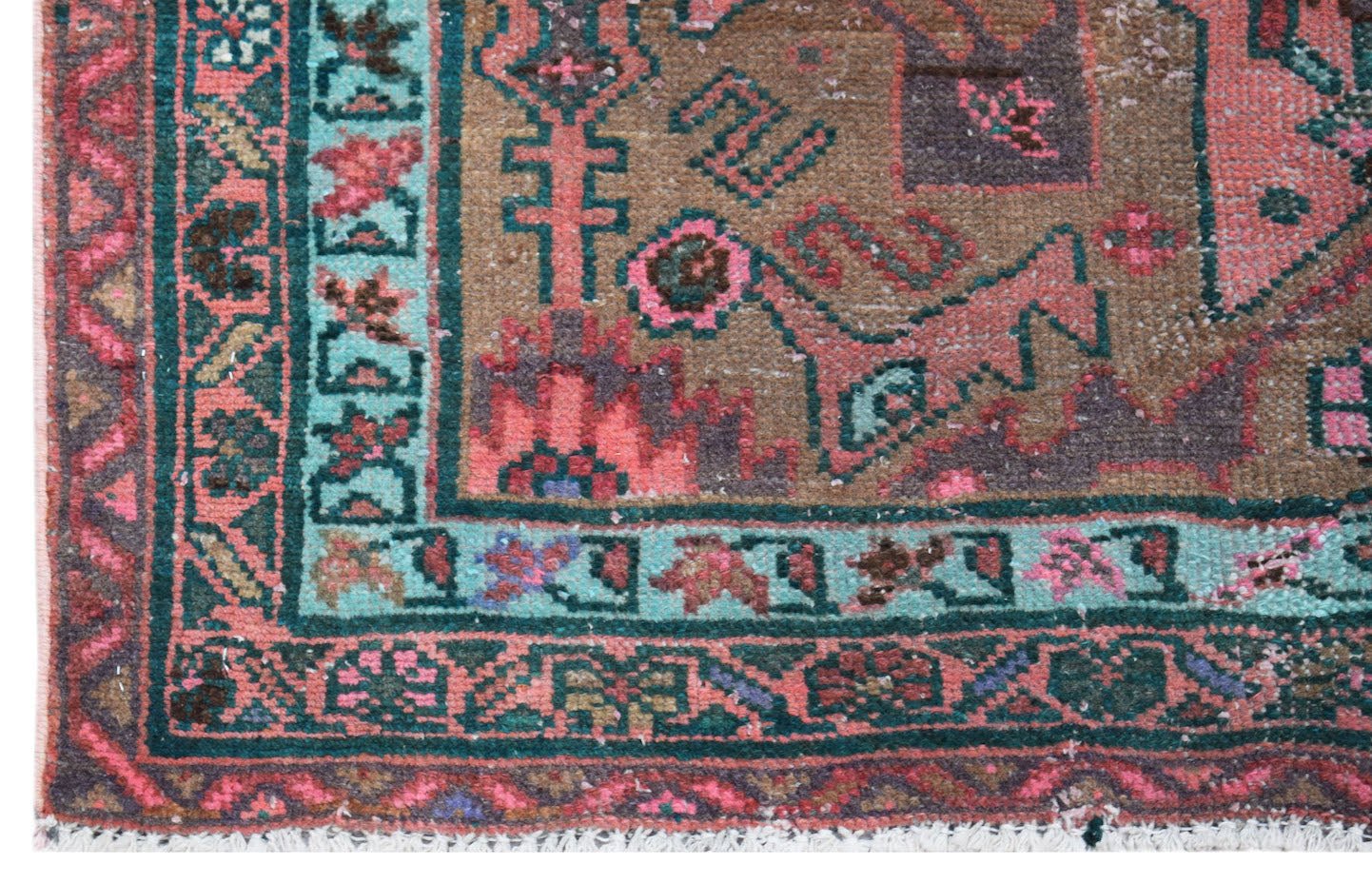A vintage handwoven Persian rug featuring a geometric pattern in shades of pink, teal, and brown.