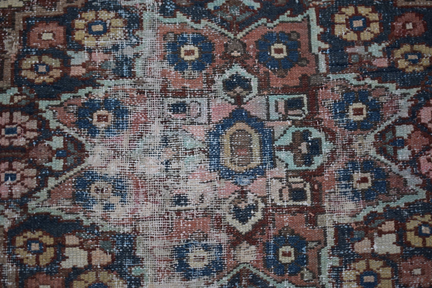 A handwoven vintage Persian rug featuring a geometric floral pattern in faded blue and red tones.