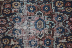 A handwoven vintage Persian rug featuring a geometric floral pattern in faded blue and red tones.