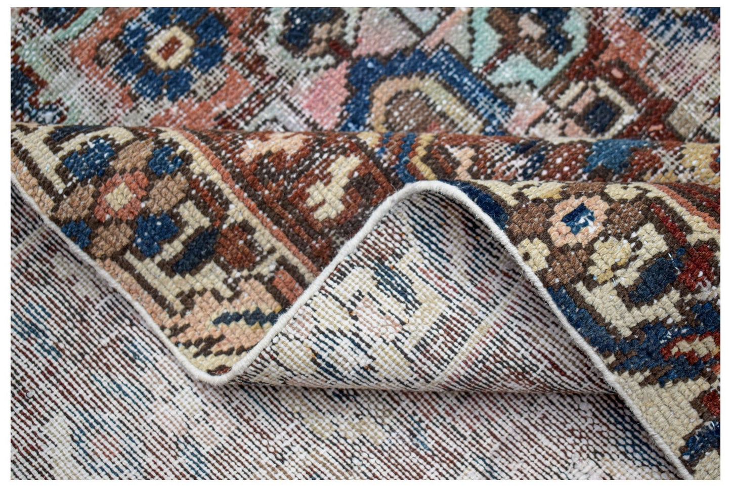 A folded vintage Persian rug featuring intricate geometric patterns in blue, red, and beige tones.