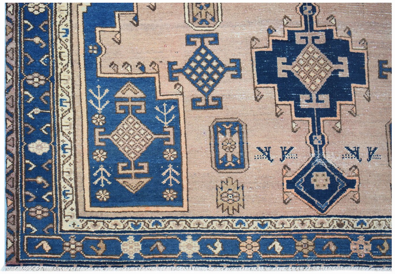 A handwoven vintage Persian rug featuring geometric blue and tan patterns on a wool pile.