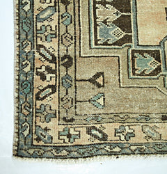 A vintage handmade Persian rug featuring geometric patterns in muted blue, brown, and beige tones.