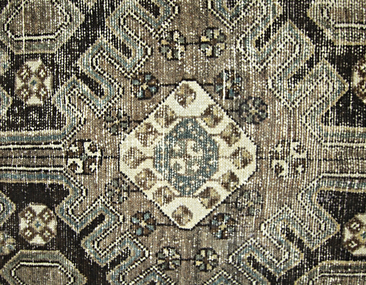 A vintage Persian rug featuring a geometric diamond pattern in shades of brown, cream, and blue.