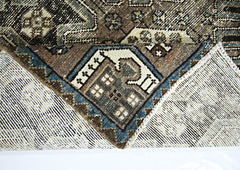 A vintage handmade Persian rug with a geometric pattern in brown, blue, and cream wool.