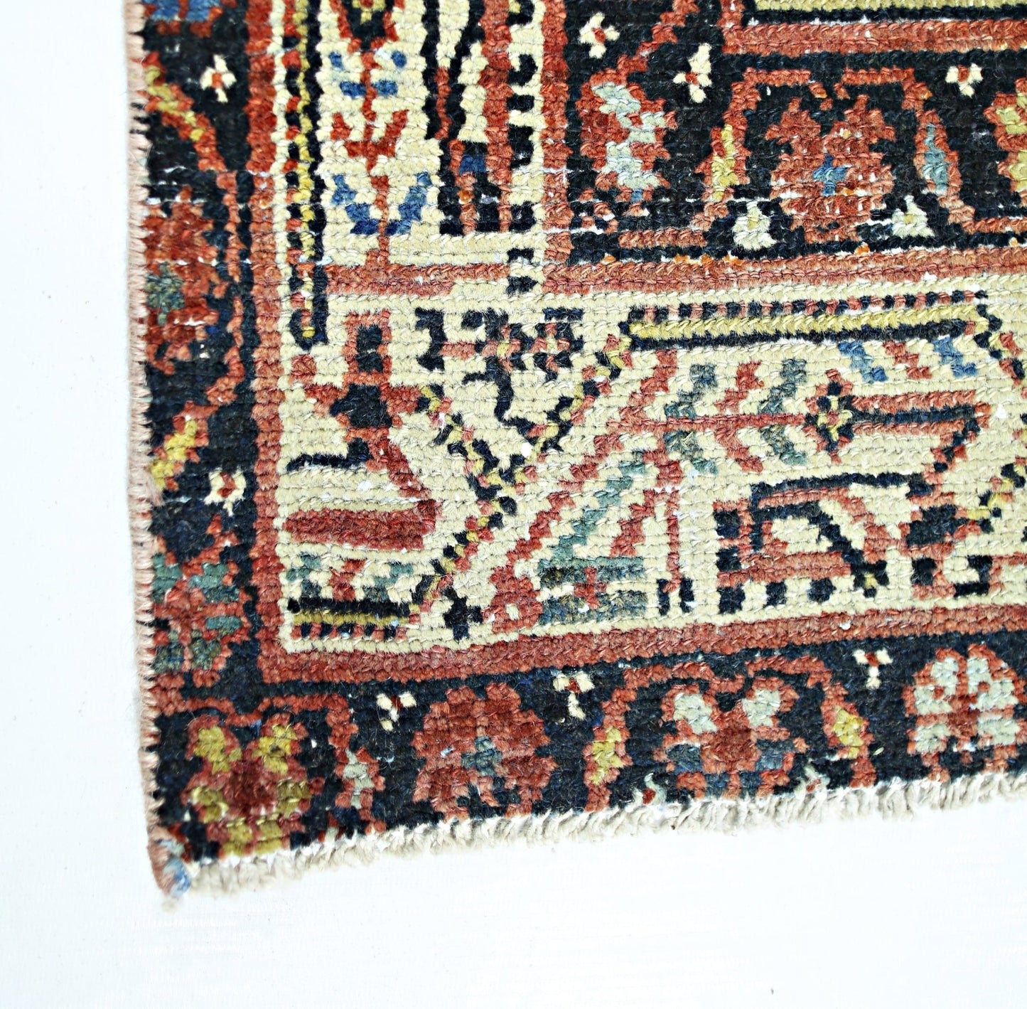 A corner view of a vintage handmade Persian rug featuring intricate geometric patterns in wool.