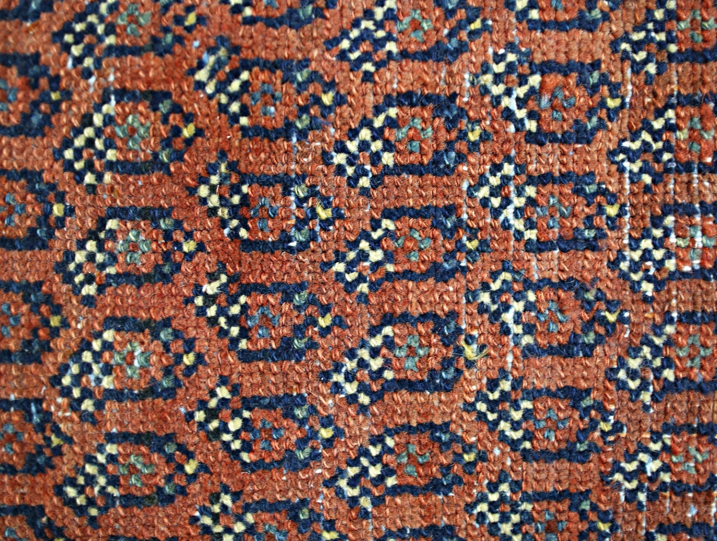 A close-up of a vintage Persian rug featuring a repeating geometric pattern in rust, blue, and gold.