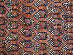 A close-up of a vintage Persian rug featuring a repeating geometric pattern in rust, blue, and gold.