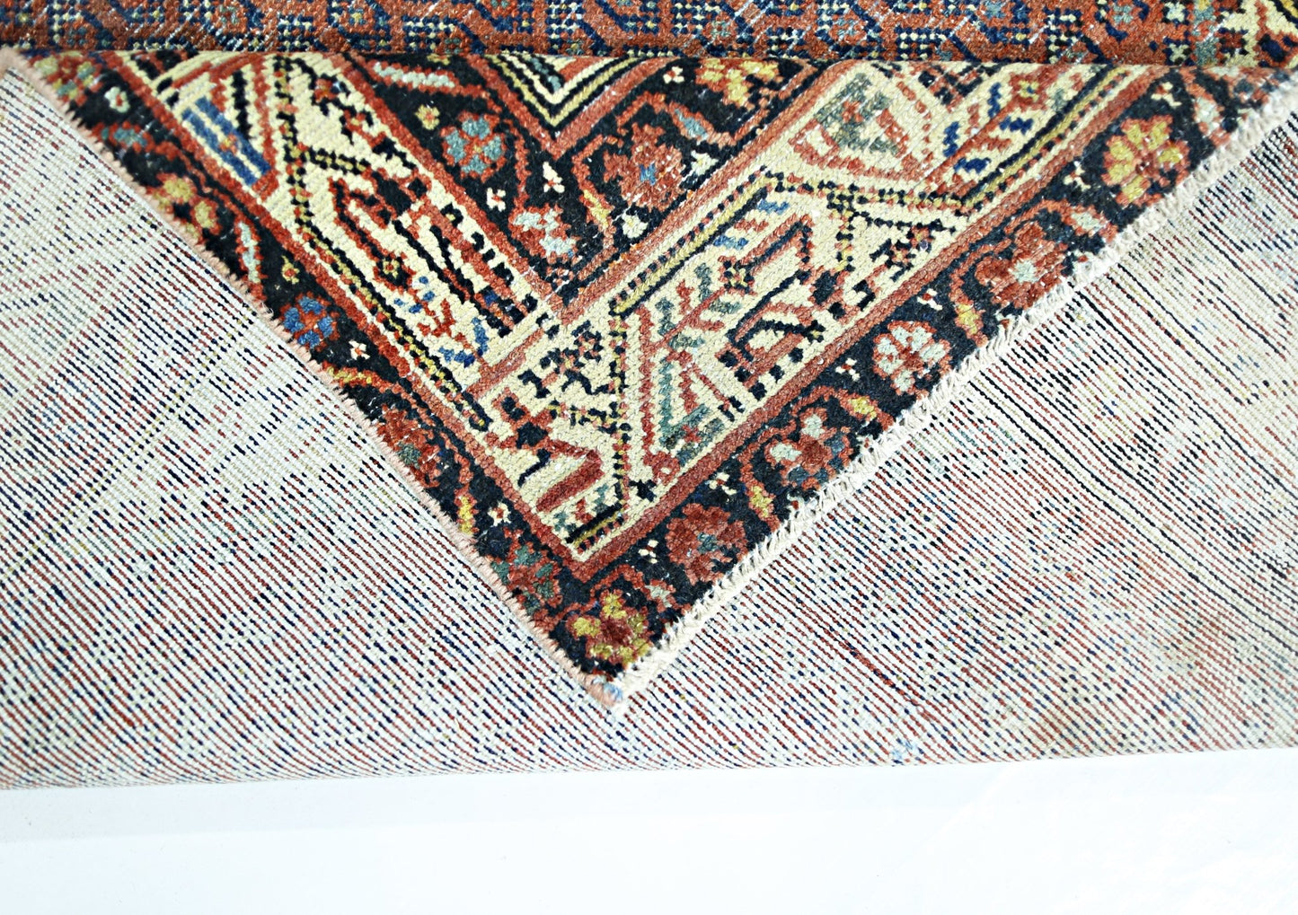 A corner of a vintage Persian rug is folded back to reveal its intricate wool pile and cotton base.