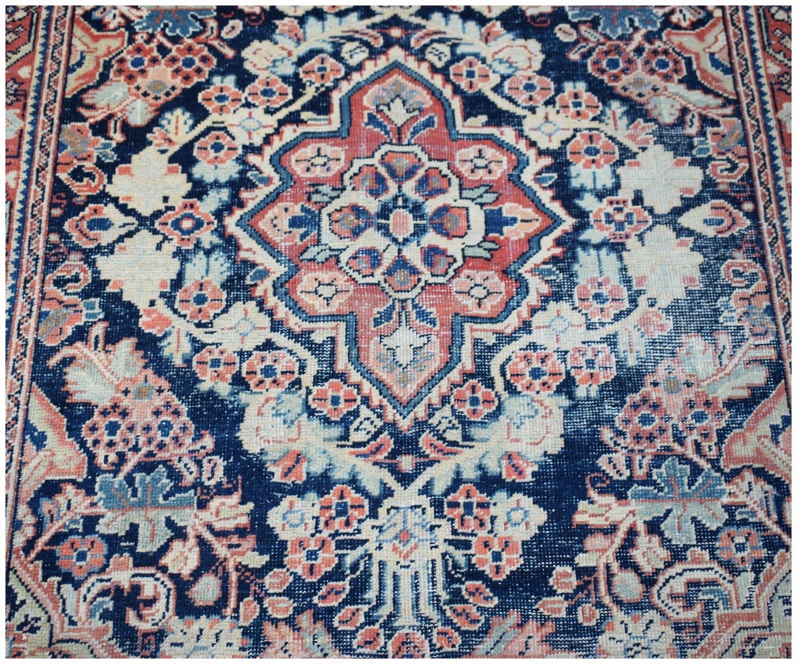 A vintage handwoven Persian rug featuring a central floral medallion on a deep blue background.
