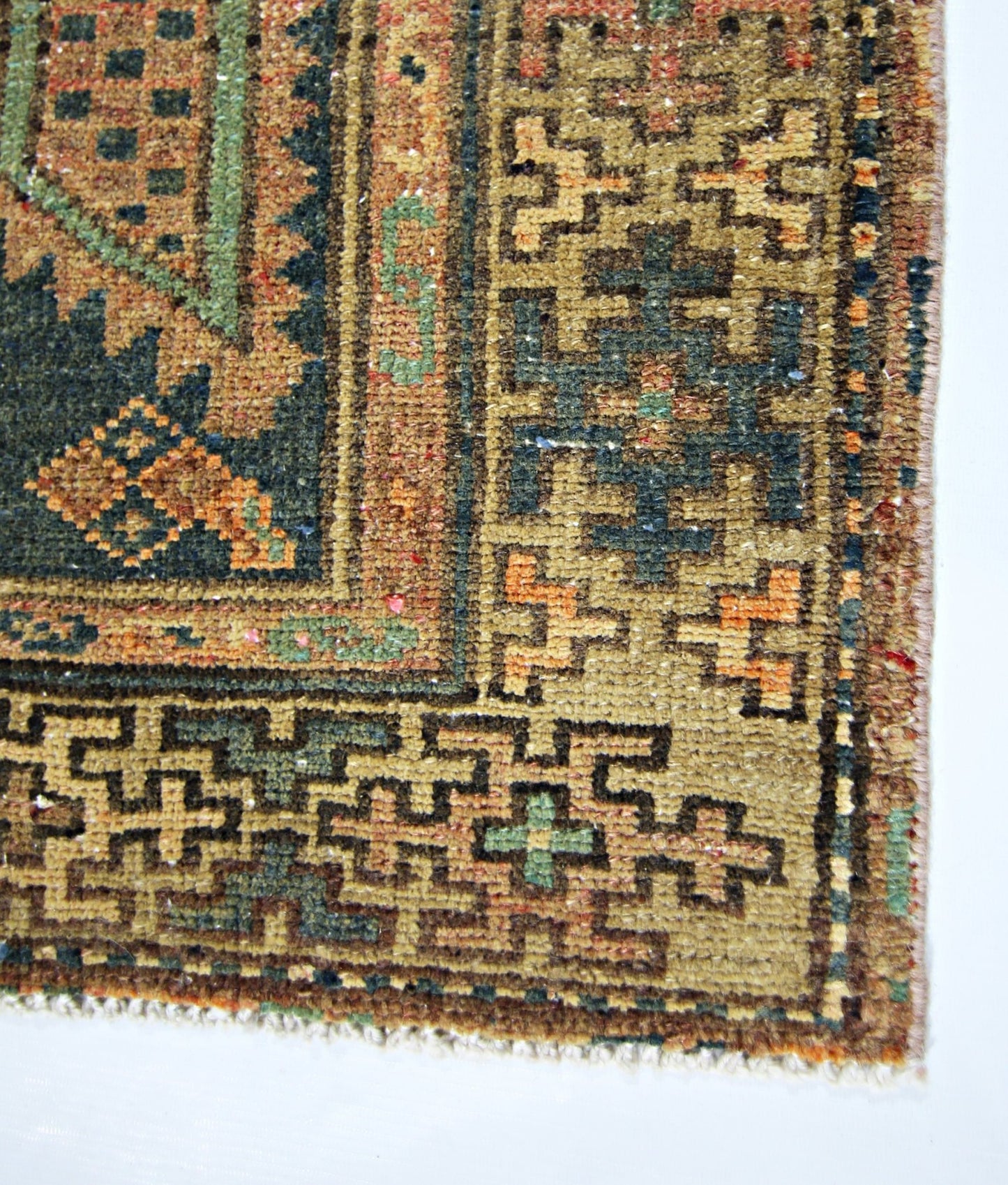 A close-up of a vintage Persian rug featuring geometric patterns in green, orange, and brown.