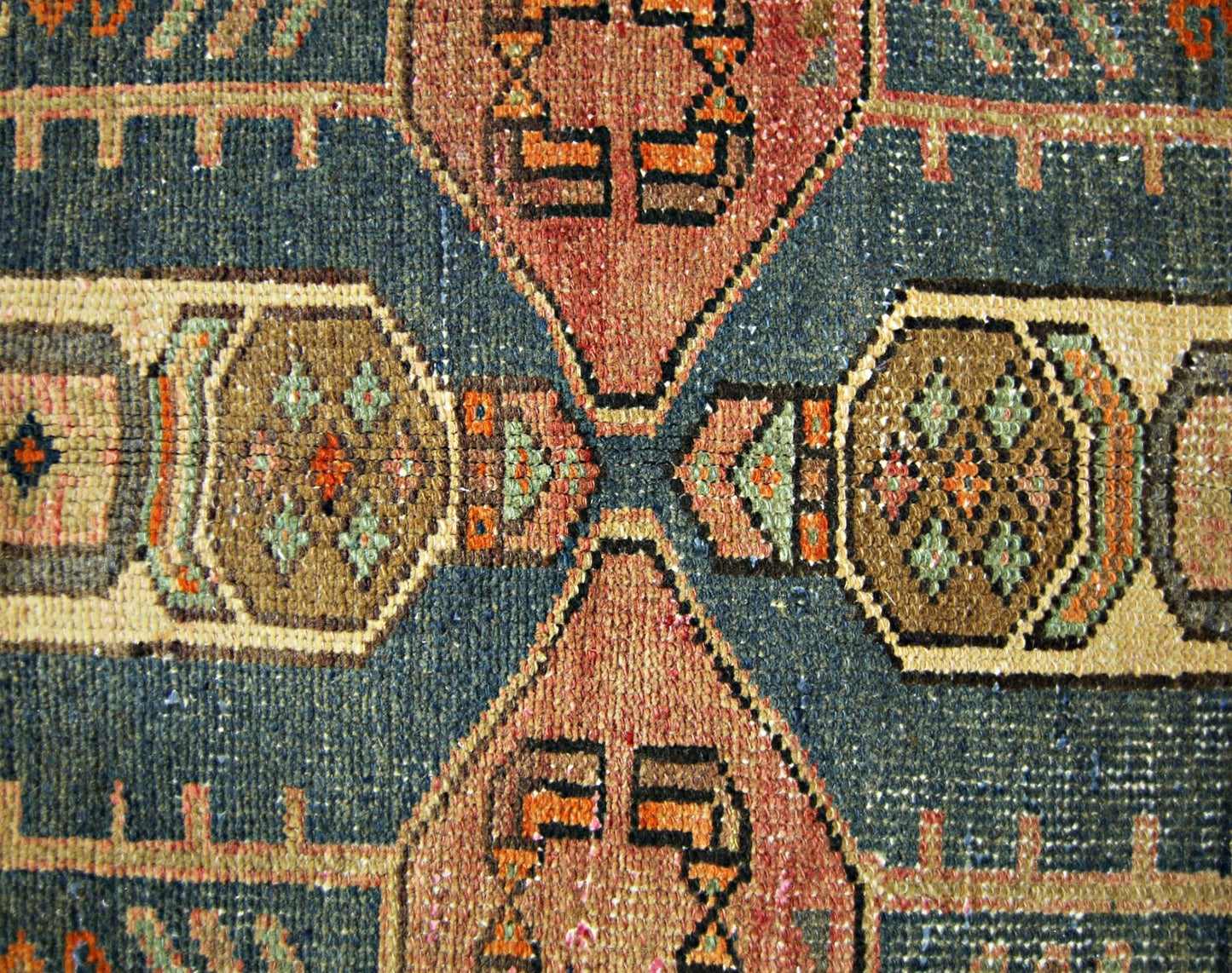A close-up of a vintage Persian rug featuring geometric patterns in blue, brown, and orange.