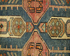 A close-up of a vintage Persian rug featuring geometric patterns in blue, brown, and orange.