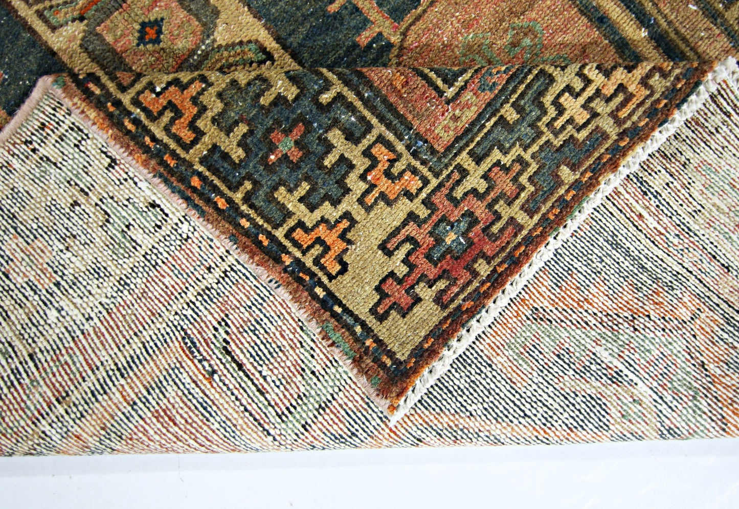 A corner of a vintage handmade Persian rug is folded back to reveal its wool pile and cotton base.