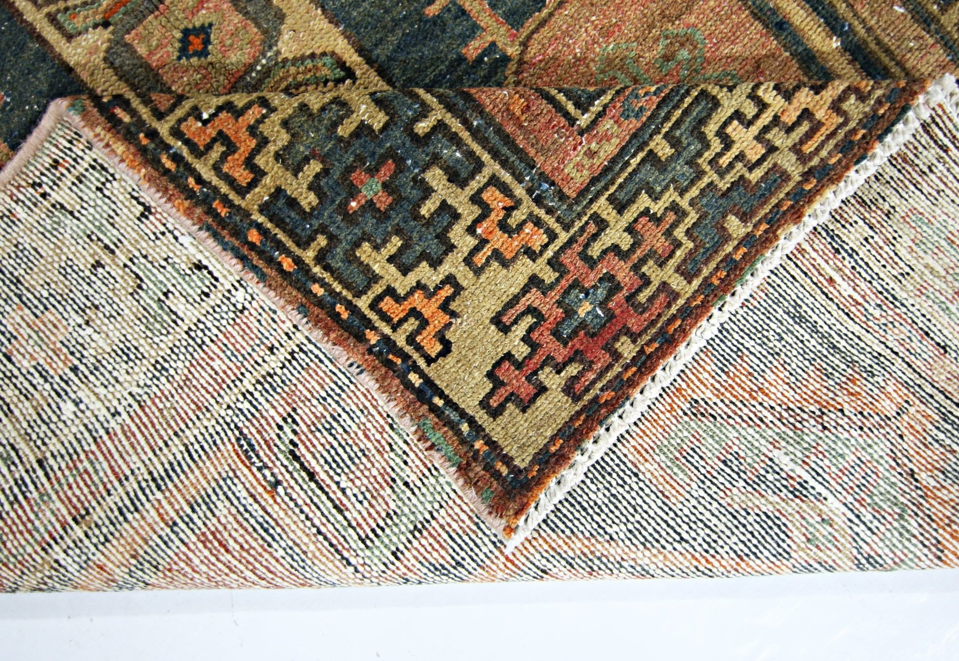 A corner of a vintage handmade Persian rug is folded back to reveal its wool pile and cotton base.