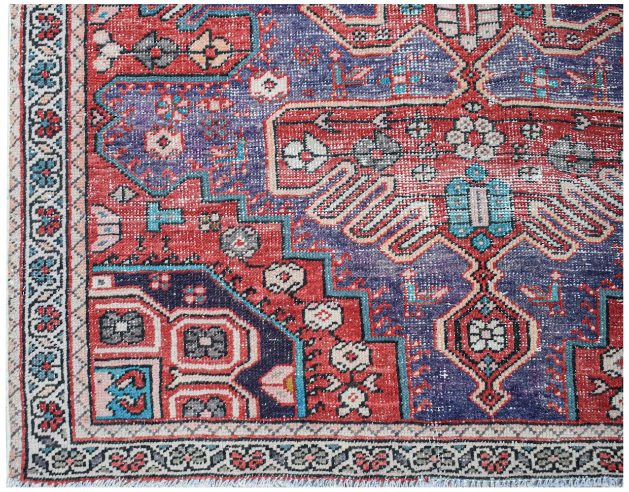 A handwoven vintage Persian rug featuring a geometric floral pattern in red, blue, and cream.