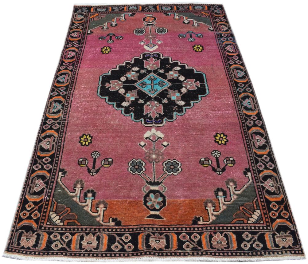A handmade vintage Persian rug featuring a central black medallion on a vibrant pink field.