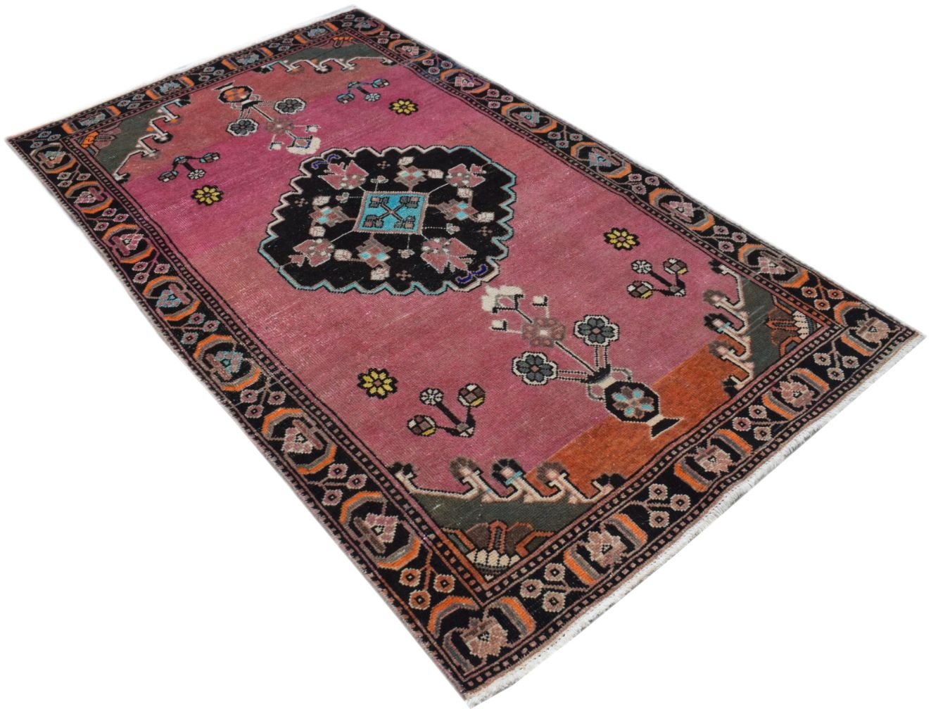 A handmade vintage Persian wool rug featuring a pink field with a central black medallion.